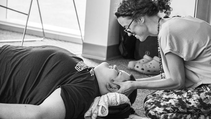 One on one practice: Sam kneeling beside a participant lying on a mat, gently supporting their head