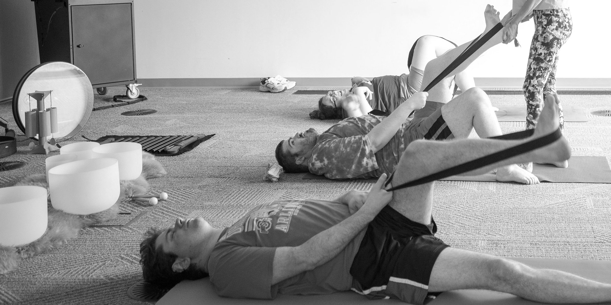 Participants lying on mats stretching a leg with a yoga strap, crystal singing bowls alongside